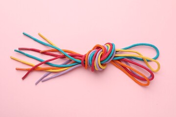 Fototapeta premium Colorful ropes tied in knot on light pink background, top view. Unity concept