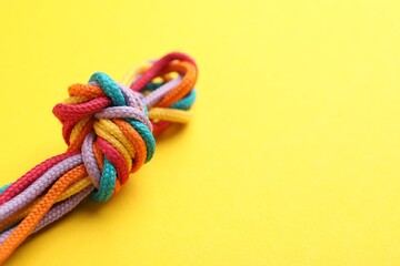 Colorful ropes tied in knot on yellow background, closeup with space for text. Unity concept