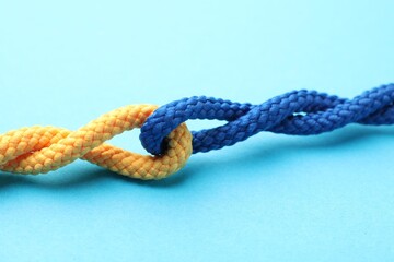Colorful ropes tied together on light blue background, closeup. Unity concept
