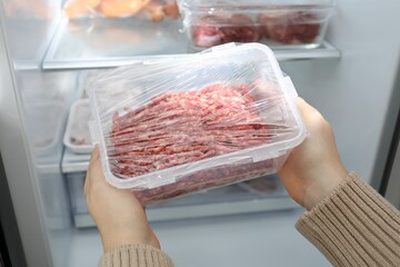 Woman taking frozen minced meat out of fridge, closeup