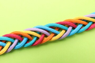 Braided colorful ropes on light green background, top view. Unity concept