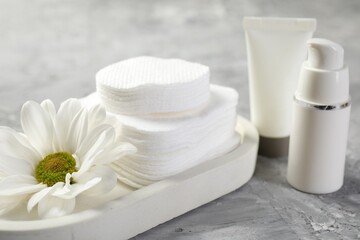 Clean cotton pads, cosmetic products and flower on grey table, closeup