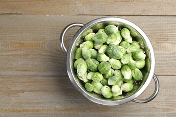 Fresh Brussels sprouts in metal colander on wooden table, top view. Space for text