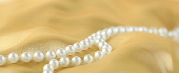 Beautiful pearl necklace on golden silk, closeup