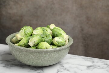 Fresh Brussels sprouts in bowl on white marble table, space for text