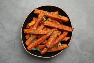 Delicious sweet potato fries with spices in bowl on grey table, top view