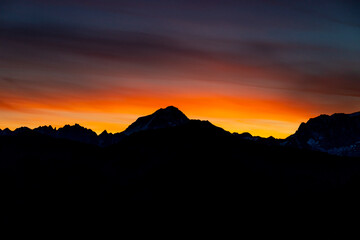 Sunset burning red and orange sky above the snow summits and rocky peaks of the Alps. Beautiful mountain sunset and sunrise in Chamonix valley on the ascent to Montblanc