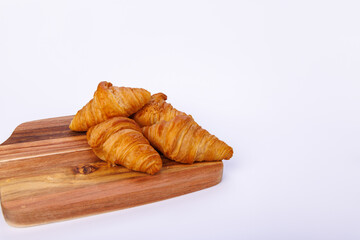 Freshly baked croissants on a wooden cutting board against a white background, showcasing a detailed view of the golden, flaky pastry