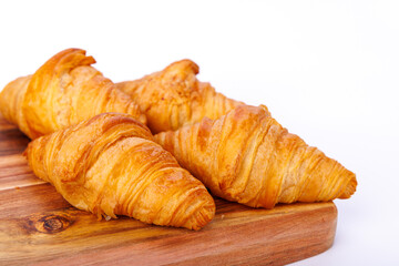 Golden, flaky croissants on a rustic wooden cutting board with a clean white backdrop, capturing detailed layers of the freshly baked pastries