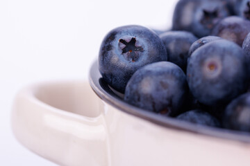 Small ceramic pot full of fresh blueberries on a seamless white background, detailed close-up