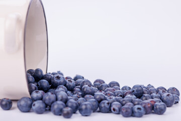 Close-up of blueberries spilling from an overturned bowl, creating a vibrant display on a white infinite background, highlighting the fruit's freshness