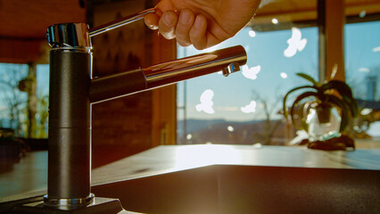 CLOSE UP: Human hand turning on kitchen faucet handle to let clean water flow through. Golden...