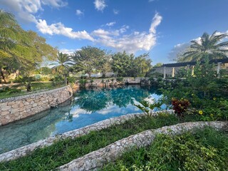 Cenote swimming pool, azure water, stone walls, blue sky with clouds, palm trees, in Merida, Yucatan Pensinsula, Mexico, November