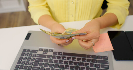 Woman counting money over a laptop keyboard. Handheld money being numbered by an accountant.