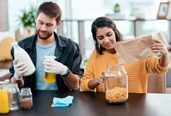Cereal, jar and sanitizing with interracial couple in kitchen of home together to organize food or groceries. Cleaning, glass or paper bag with man and woman in apartment for diet, health or wellness