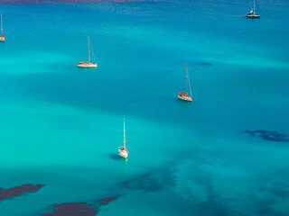Turquoise waters surround anchored sailboats off the coast of Sardinia, Italy. The gradient of blue...
