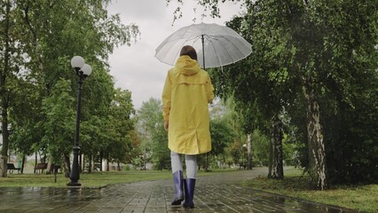 girl under umbrella. Slow motion. rain city park. view from back. young woman hiding under umbrella...