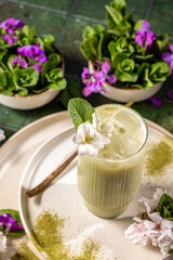 Iced matcha latte garnished with mint and flowers on table setting