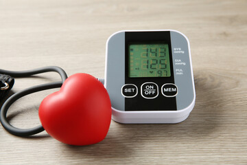 Blood pressure measuring device and squeeze heart on wooden table, closeup