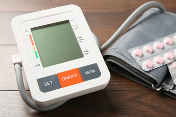 Blood pressure measuring device and pills on wooden table, closeup