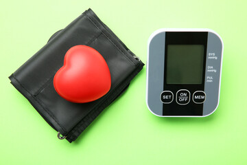 Blood pressure measuring device and squeeze heart on green background, top view