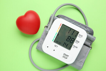 Blood pressure measuring device and squeeze heart on green background, top view