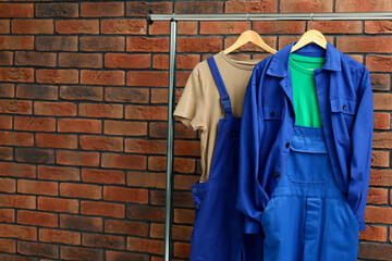 Workers' uniforms on clothing rack near brick wall, space for text