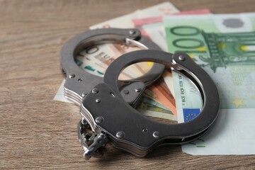 Corruption. Handcuffs and euro banknotes on wooden table, closeup