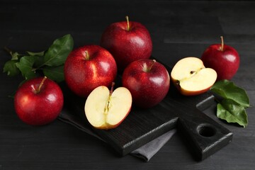 Fresh ripe red apples and green leaves on black wooden table