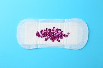 Menstrual pad and sequins on light blue background, top view