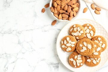 Tasty cookies with almond flakes and nuts on white marble table, top view. Space for text