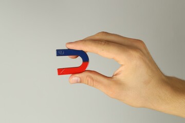 Man holding horseshoe magnet on grey background, closeup