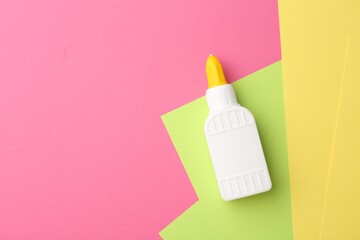 Bottle of glue and colorful paper on pink background, top view. Space for text