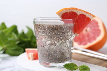 Glass of drink with chia seeds and grapefruit on white marble table, closeup