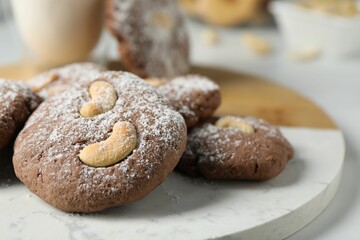 Tasty chocolate cookies with cashew and powdered sugar on white table, closeup