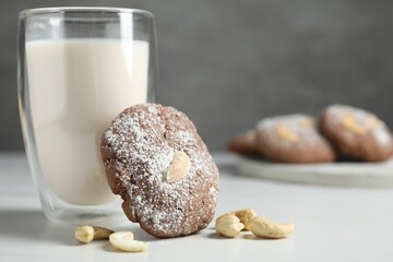 Tasty chocolate cookie with cashew and glass of milk on white table, closeup. Space for text