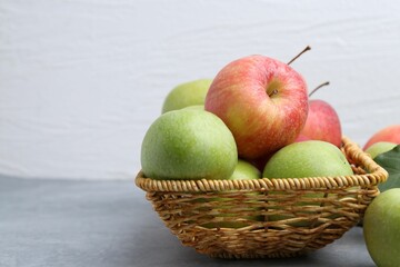 Fresh ripe apples in wicker basket on grey table, closeup. Space for text
