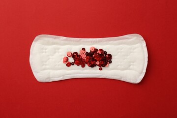 Menstrual pad with sequins on red background, top view