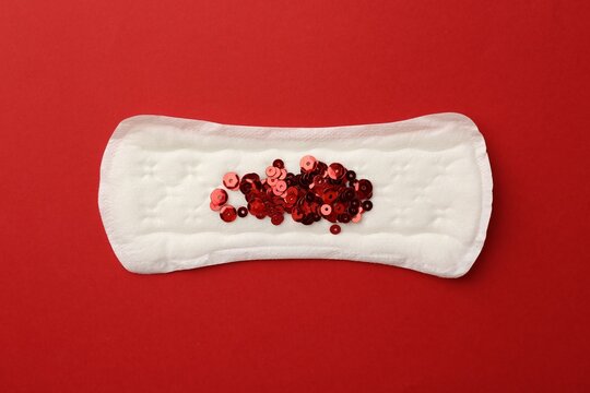 Menstrual pad with sequins on red background, top view