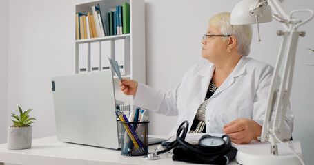 Doctor in dental clinic analysing x-ray by raising it to the window light. Dentist Checking X Ray Of Patient Teeth On Digital Screen