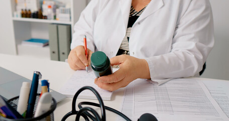 Doctor holding pill bottle and writing dosage on it. Nurse analyses doctor prescriptioned capsules.