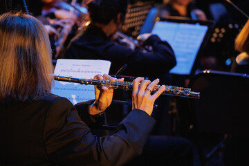 In a vibrant orchestra setting, a talented woman is skillfully playing a beautiful flute,...