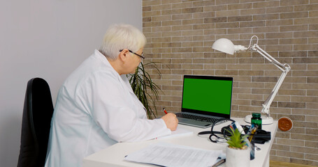 Training online done by a senior doctor taking notes in her office. Medicare assistant taking notes searching for information for her job.
