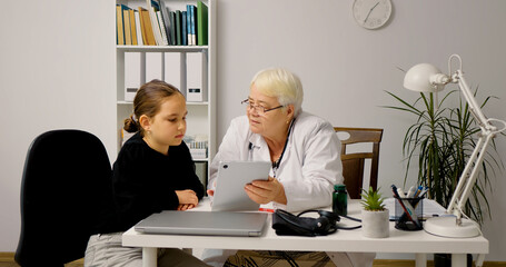 Female doctor showing results to girl on tablet screen. Concept of medical, healthcare, healthy family, pediatric checkup and hospital office.