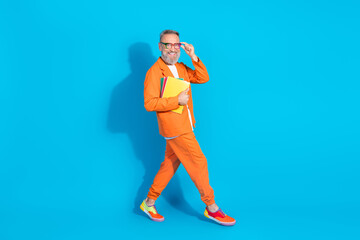 Full body portrait of modern stylish aged man hold book walk empty space wear orange costume isolated on blue color background