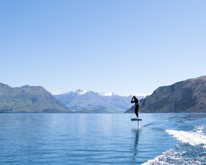 Person Foil Surfing on a Beautiful Mountain Lake. 
Snow-capped mountains and clear blue skies frame...