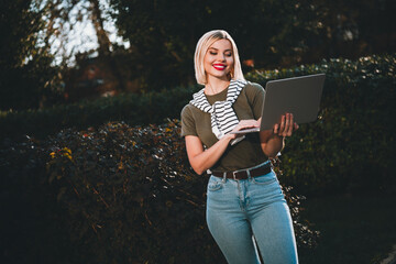 Photo of positive young blonde girl hold telephone wear khaki outfit tied shoulders sweater walk...