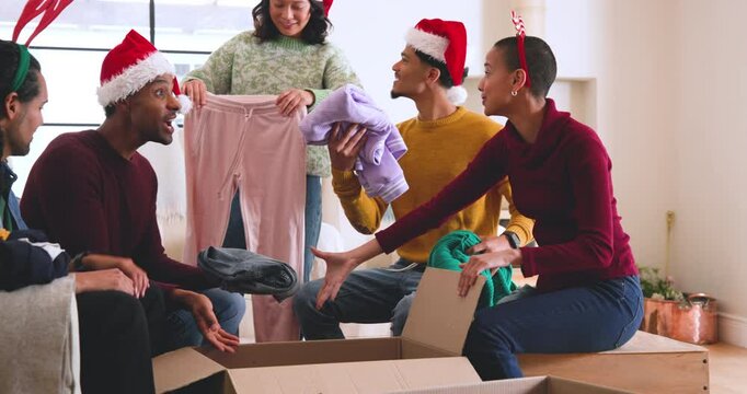 At christmas, young diverse friends wearing festive hats packing clothes for donations at home
