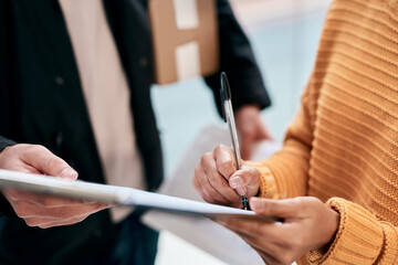 Delivery person, hands and customer with signature in home for package, parcel and courier. People, employee and paperwork with boxes for agreement or contract with online shopping and distribution