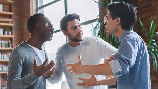 Office conflict concept. Emotional young multiracial men arguing at office